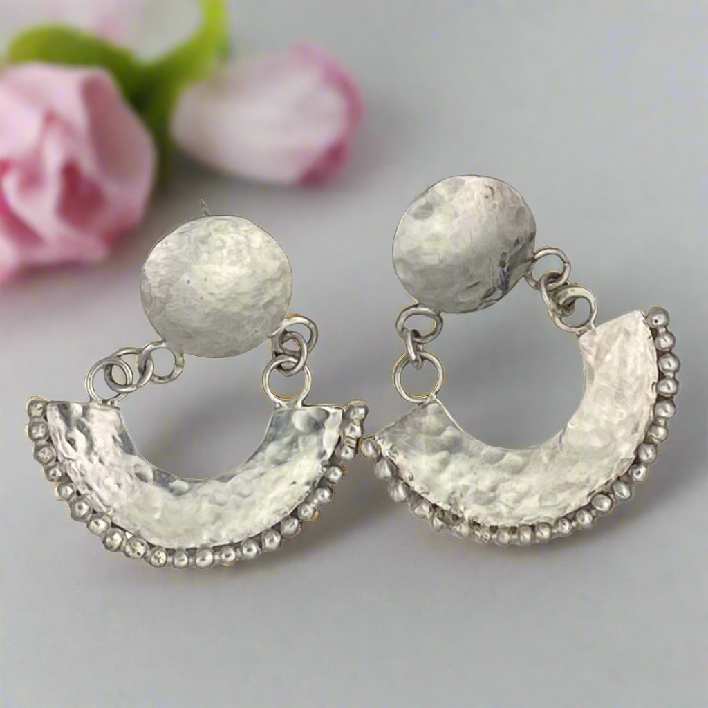 Pair of silver earrings with round top and half-circle bottom on a white background